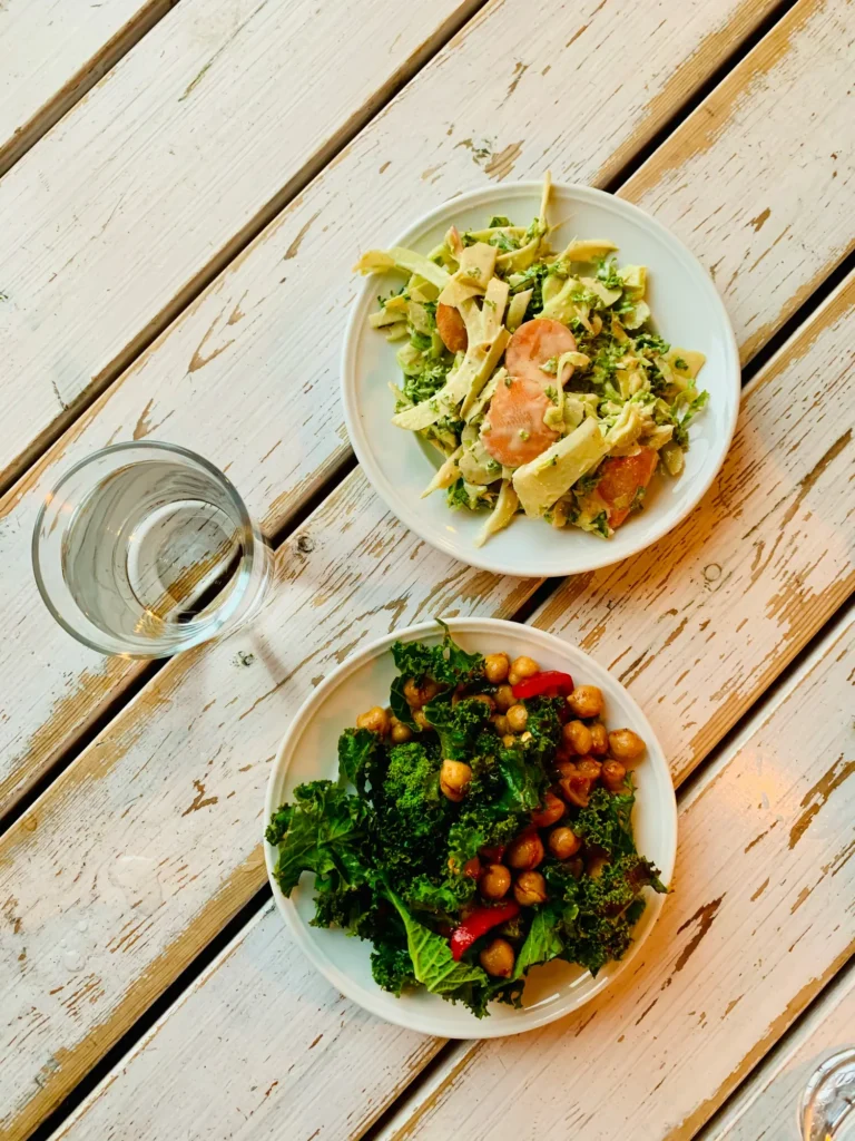 Two plates of different food on a weathered white wooden table, seen from above, with a glass of water beside them.